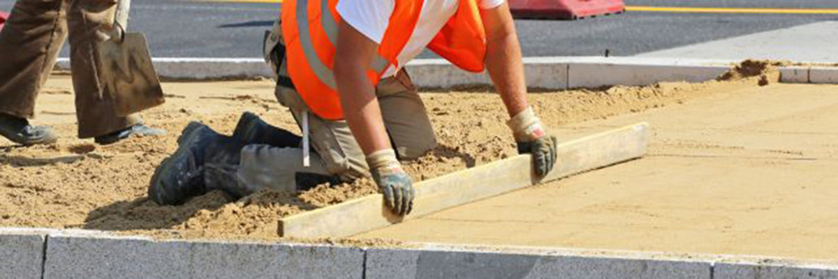 bau, baustelle, strassenbau, straßenbau, bauarbeiter, arbeiter, pflasterbett, abziehen, sand, hut, sonnenschutz, kopfbedeckung, hitze, sommer, schaufel, sandbett, steine, begrenzungssteine, bordstein, arbeitshandschuhe, signalfarbe, orange, signalweste, steinreihe, randbegrenzung, richtlatte