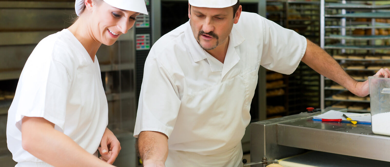Female and male baker baking fresh bread in the bakehouse, they produce brezn Schlagwort(e): Baker, bakery, man, woman, bakehouse, "baker's shop", shop, bread, brezn, pretzel, brezen, morning, oven, fresh, warm, flavor, work, working, occupation, homemade, handcraft, "Food Industry", product, products, production, quality, manufacturing, cap, workwear, "work clothes", female, male, bake, baking, people, Caucasian, sheet, tray, bcker, bckerei, bckerin, frau, mann, backstube, backofen, backen, brotofen, ofen, brot, brezn, breze, brezen, frisch, warm, morgens, duft, duften, knackig, beruf, arbeiten, arbeit, handwerk, handwerker, handwerksberuf, geselle, meister, bckermeister, meisterberuf, qualitt, lebensmittel, lebensmittelindustrie, lebensmittelverordnung, backblech, bckermtze, kittel, arbeitskleidung, produktion, herstellung, herstellungsprozess, mensch, menschen, person, leute