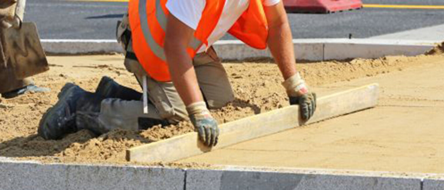 bau, baustelle, strassenbau, straßenbau, bauarbeiter, arbeiter, pflasterbett, abziehen, sand, hut, sonnenschutz, kopfbedeckung, hitze, sommer, schaufel, sandbett, steine, begrenzungssteine, bordstein, arbeitshandschuhe, signalfarbe, orange, signalweste, steinreihe, randbegrenzung, richtlatte