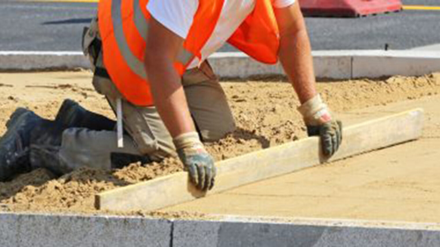 bau, baustelle, strassenbau, straßenbau, bauarbeiter, arbeiter, pflasterbett, abziehen, sand, hut, sonnenschutz, kopfbedeckung, hitze, sommer, schaufel, sandbett, steine, begrenzungssteine, bordstein, arbeitshandschuhe, signalfarbe, orange, signalweste, steinreihe, randbegrenzung, richtlatte